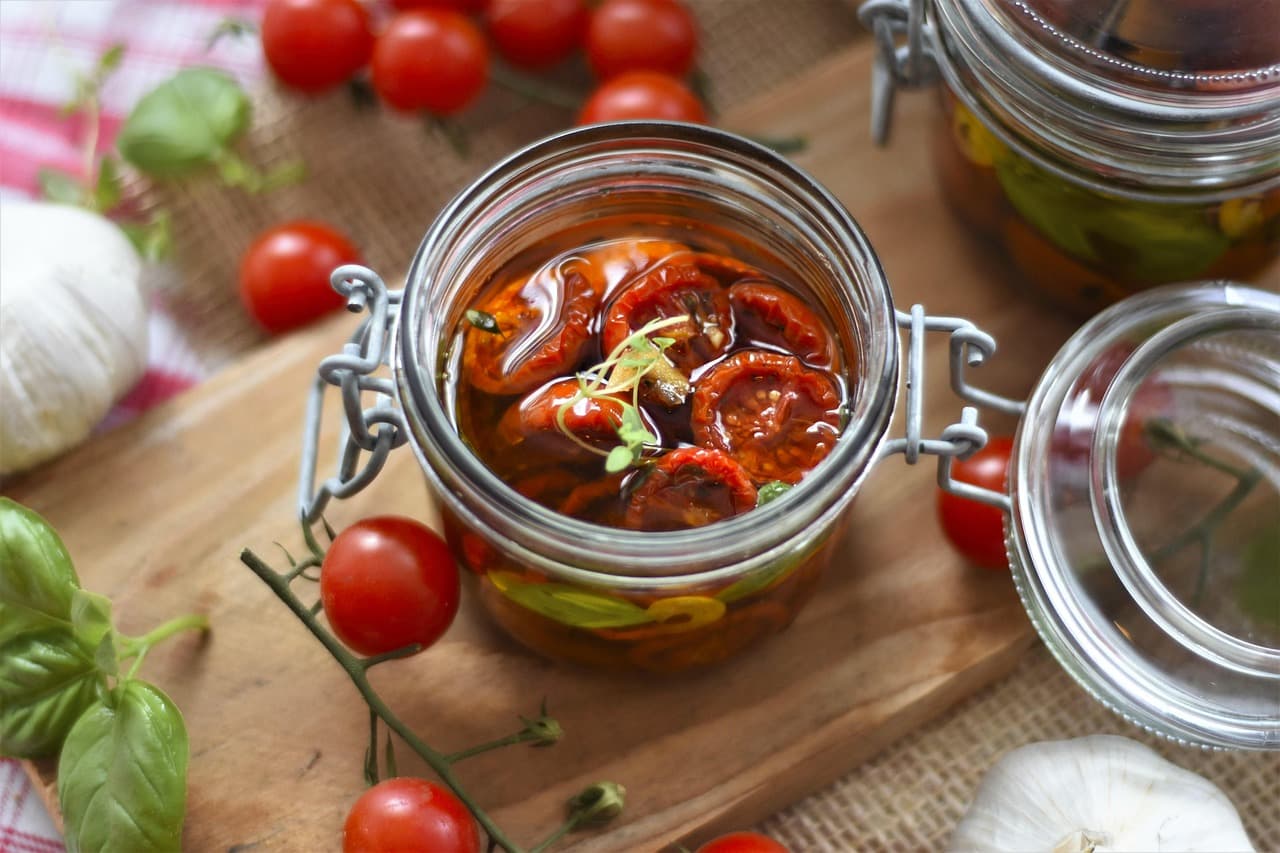 Sun-dried tomatoes in a glass jar with fresh tomatoes and basil