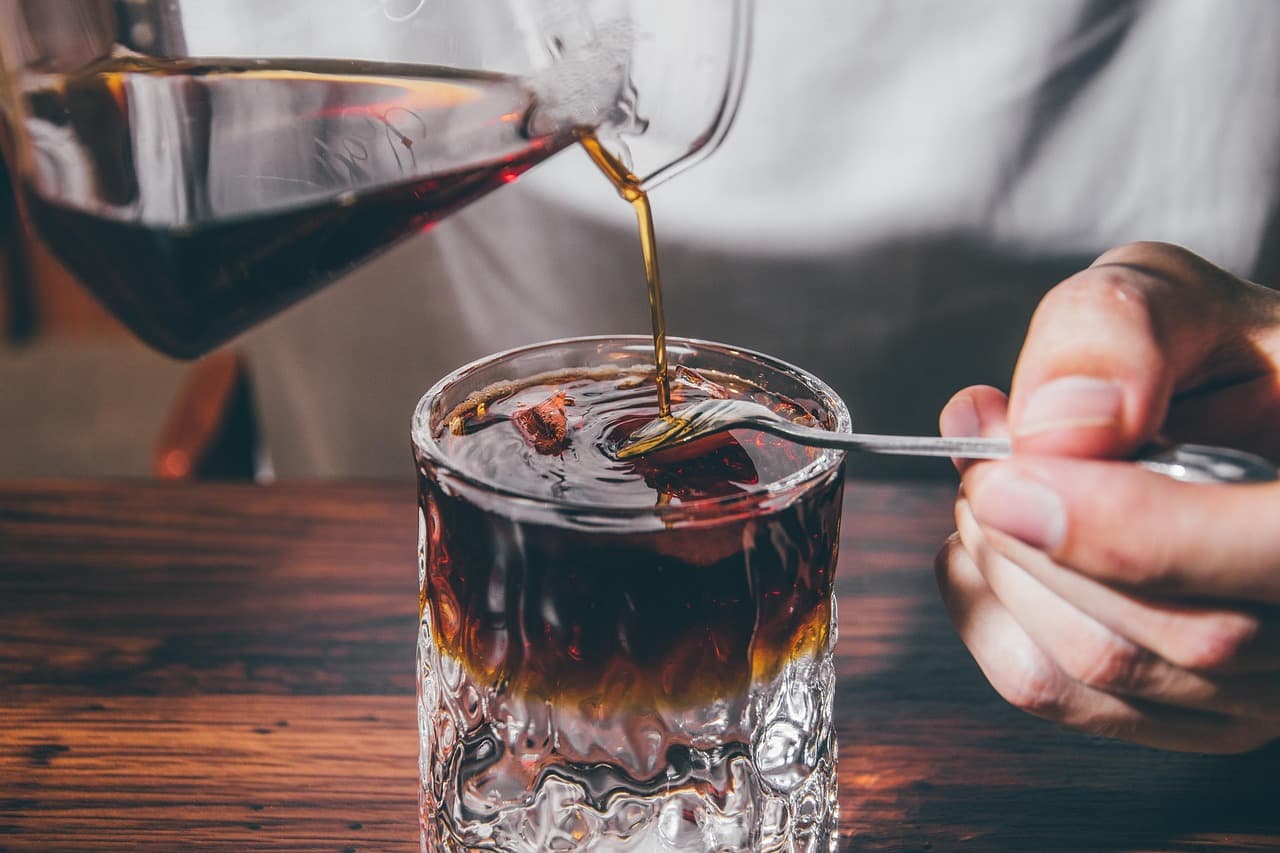 Iced coffee being poured over ice in a glass