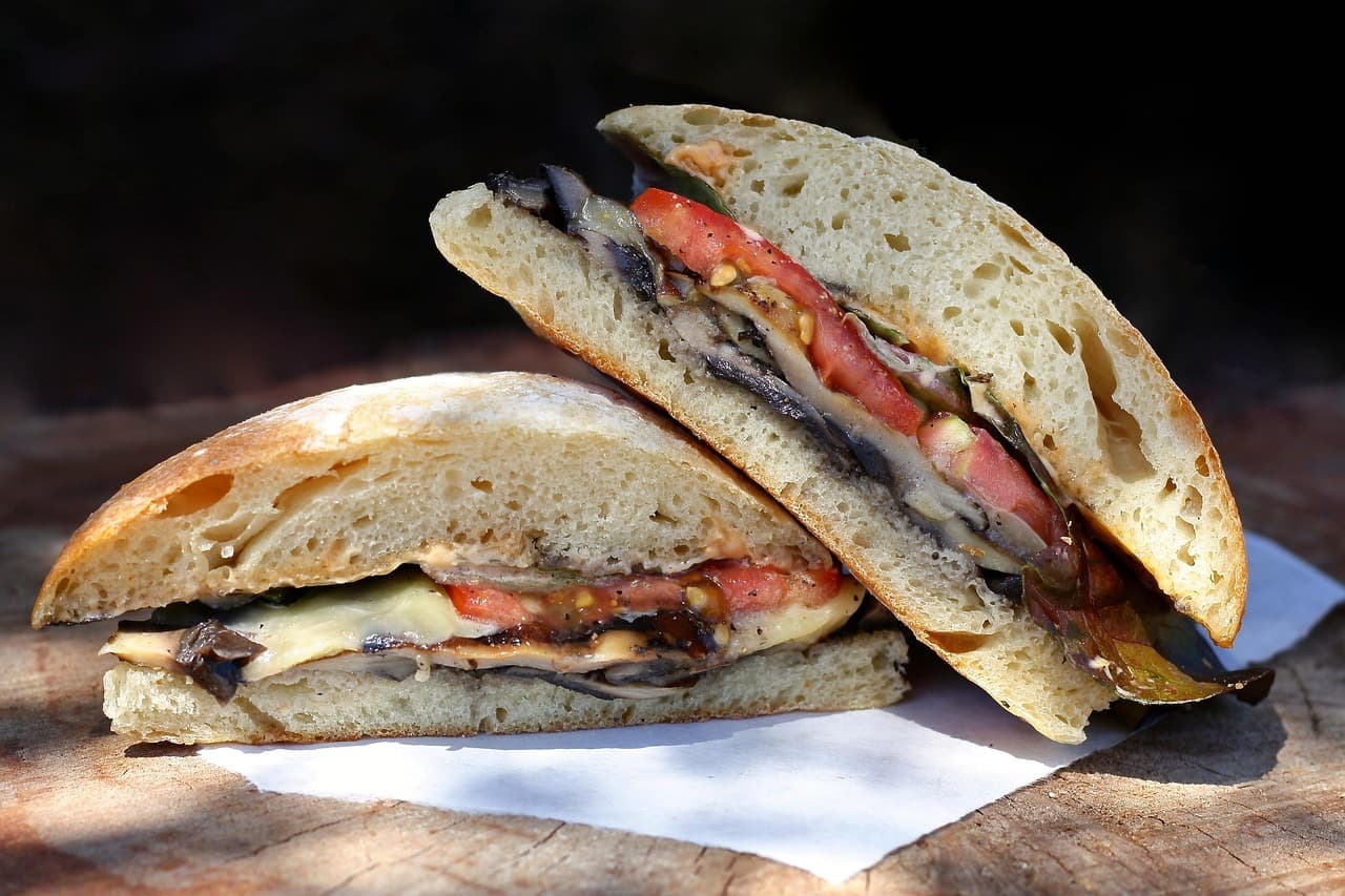A ciabatta sandwich cut in half, filled with grilled vegetables, tomato and melted cheese