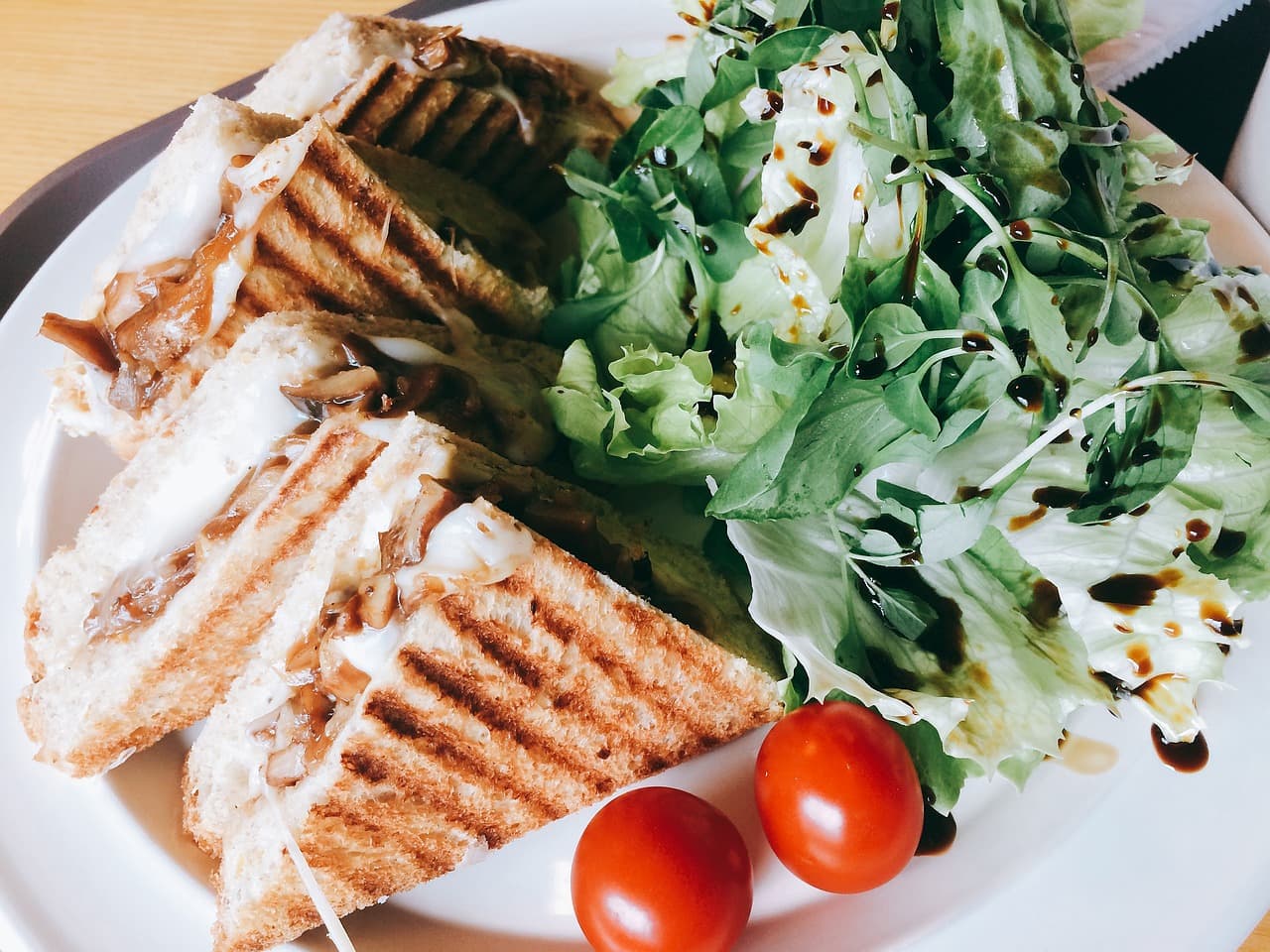 A toasted panino cut into halves with salad leaves, balsamic and cherry tomatoes