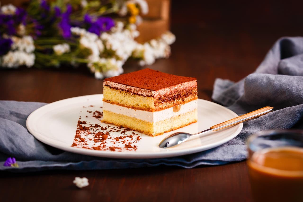 A slice of tiramisu dusted with cocoa on a white plate