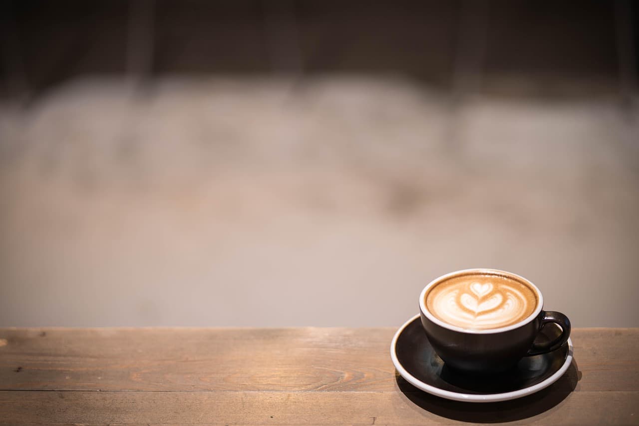 A small cappuccino on a saucer at the end of a wooden counter