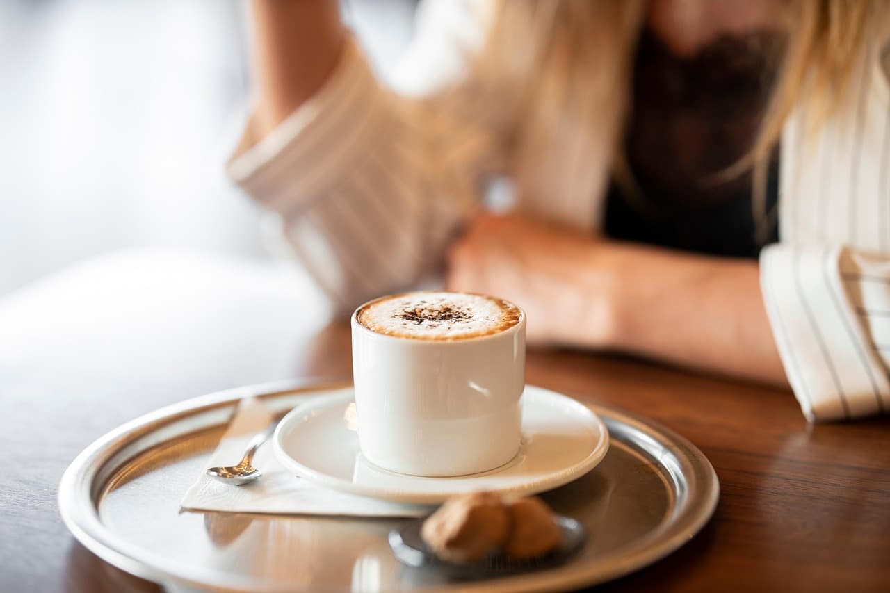 A cappuccino on a silver tray with a spoon and a biscuit