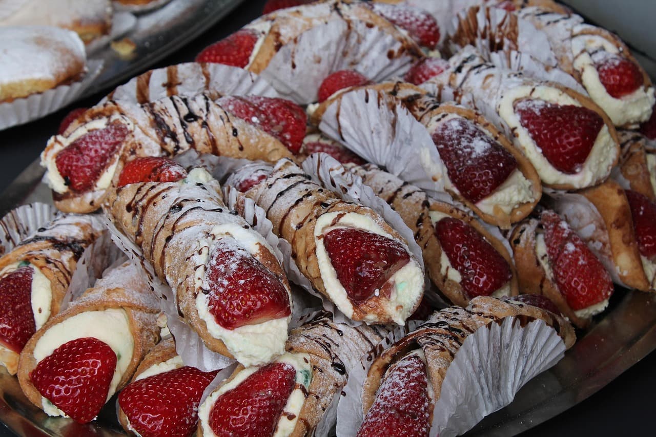 A tray of cannoli filled with cream and strawberries